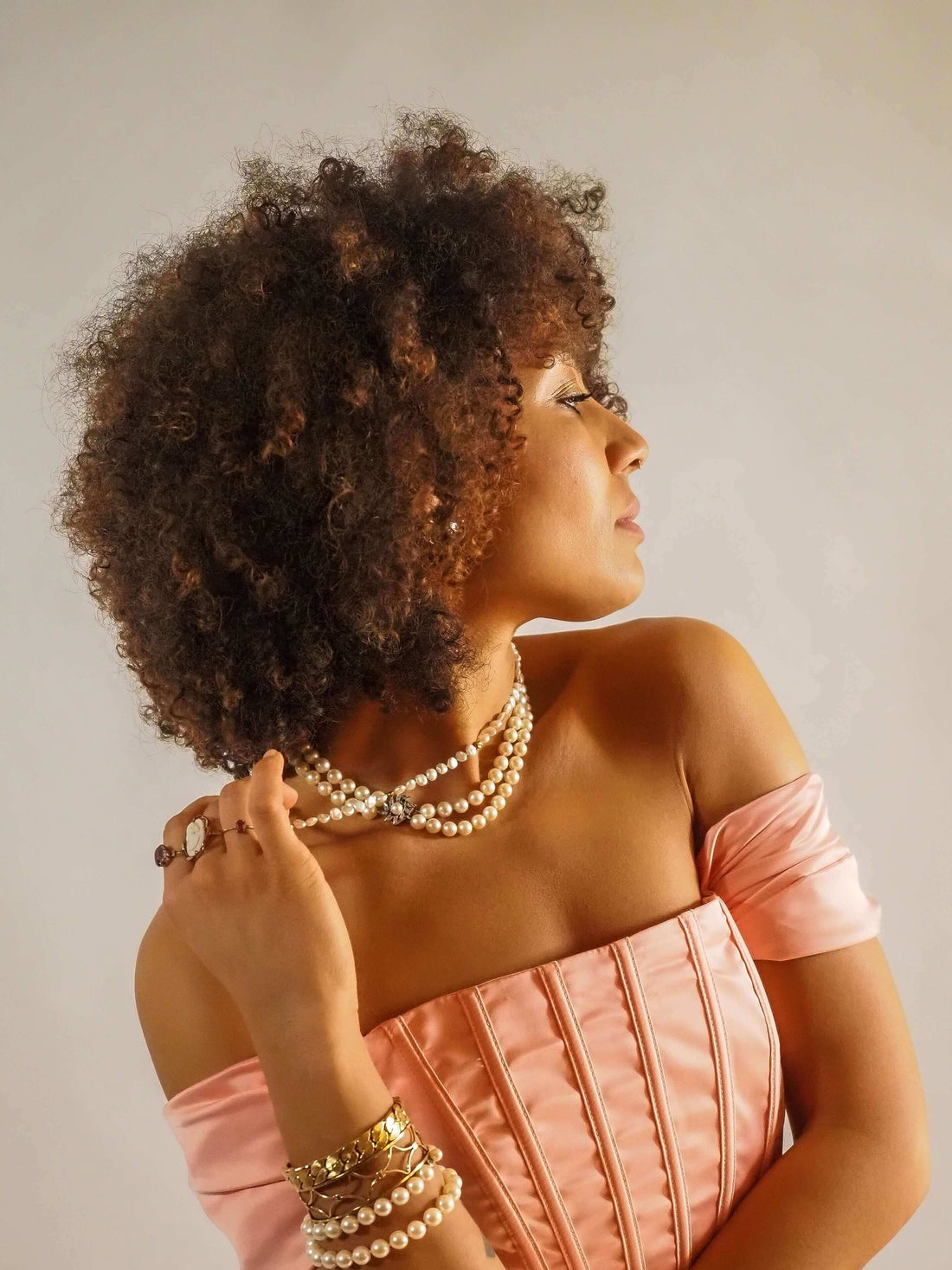 a woman wearing a strapless pink dress wearing lots of pearl jewelry holds the necklace between her fingers
