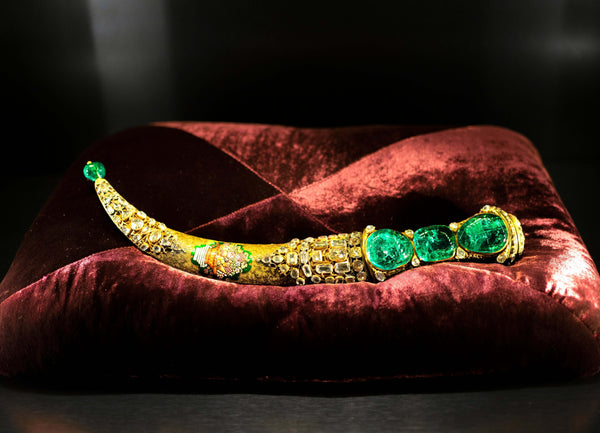 a long gold dagger encrusted with green gemstones on a red table