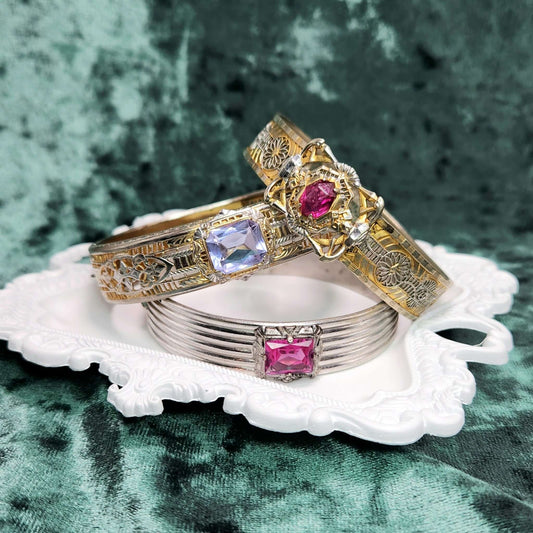 stack of colorful filigree bangles in pink and purple on a white tray on green velvet