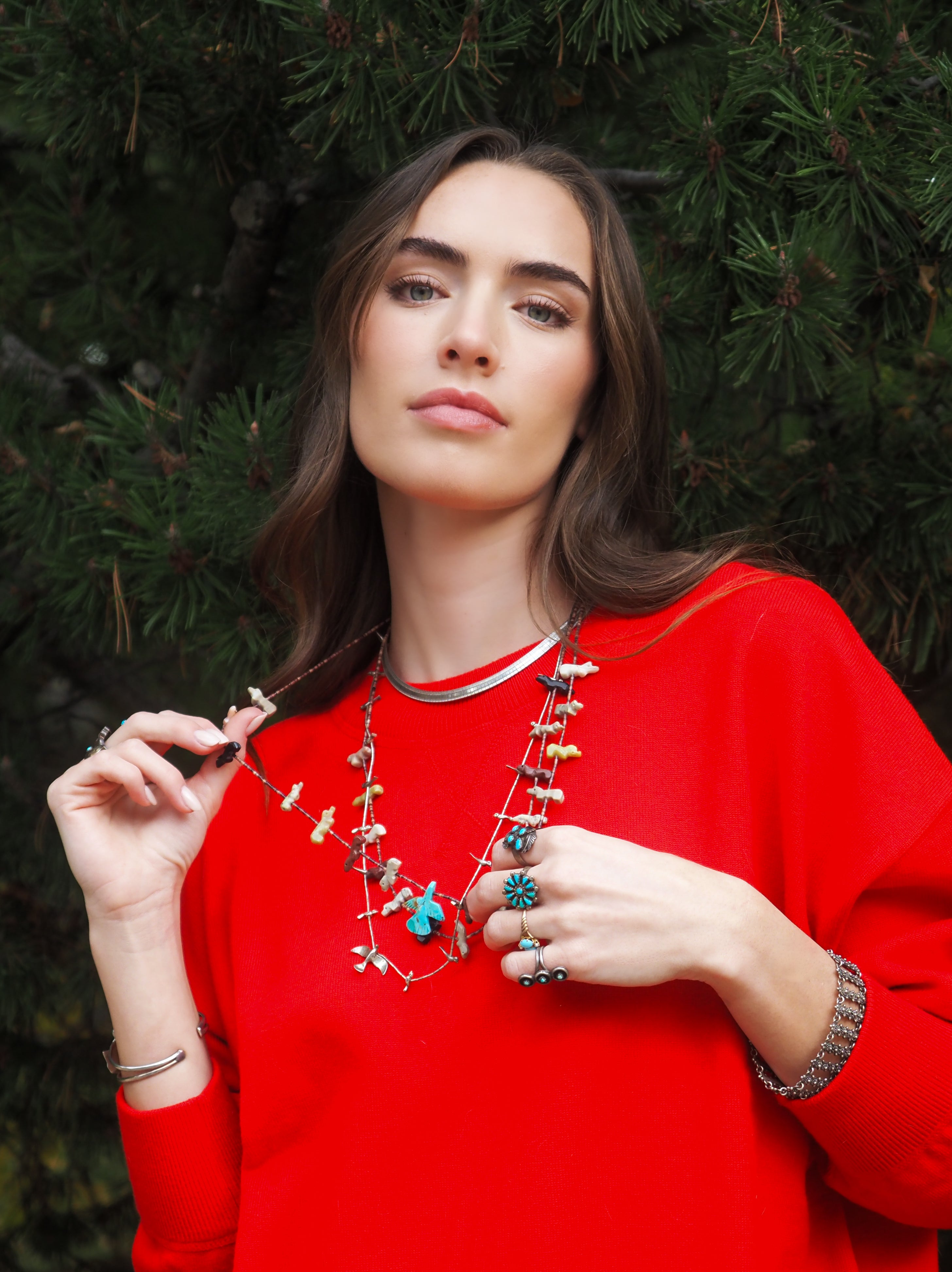 Woman wearing a red sweater and colorful jewelry against a green foliage background