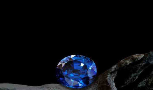 a bright blue oval cut gemstone against a dark rock and black background