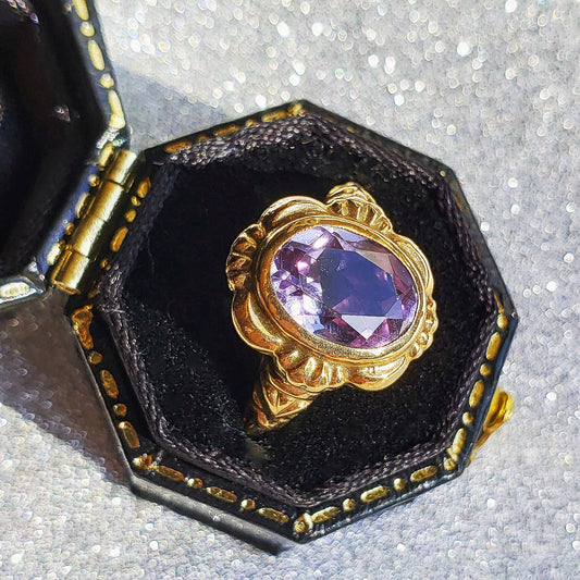 color change purple spinel gold ring in a black octagonal box with a silver sparkly back ground