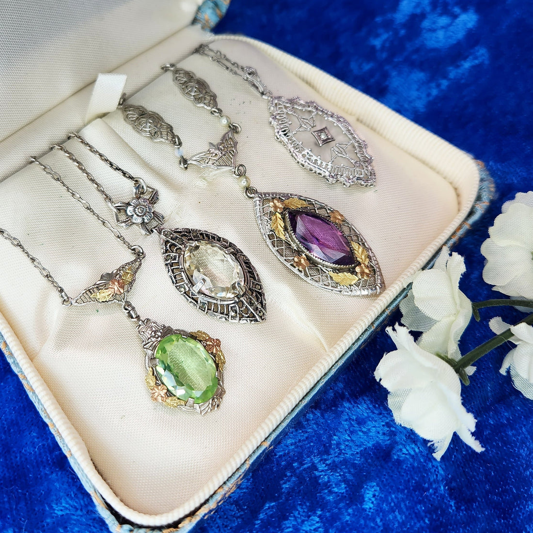 four necklaces in a white jewelry box on blue velvet with white flower