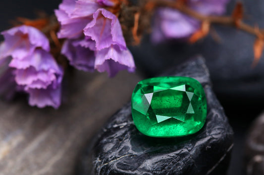 Large green gemstone on a black rock with purple flowers in the back ground