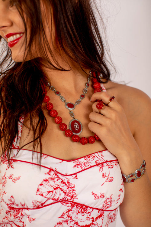 A brown haired woman wearing a red and white dress with red jewelry on her neck and wrist
