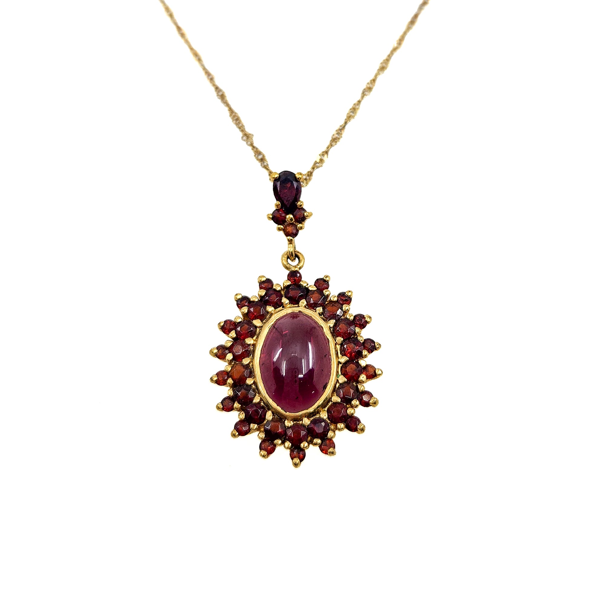 A gold pendant necklace featuring a central oval ruby cabochon surrounded by a sunburst of smaller round red gemstones, suspended from a delicate gold chain on a plain white background.