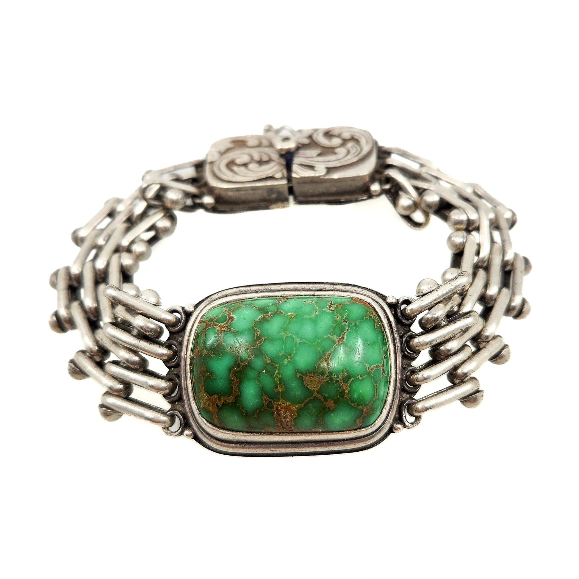 A silver-toned cuff bracelet featuring a rectangular green turquoise stone with brown matrix, set against a plain white background.