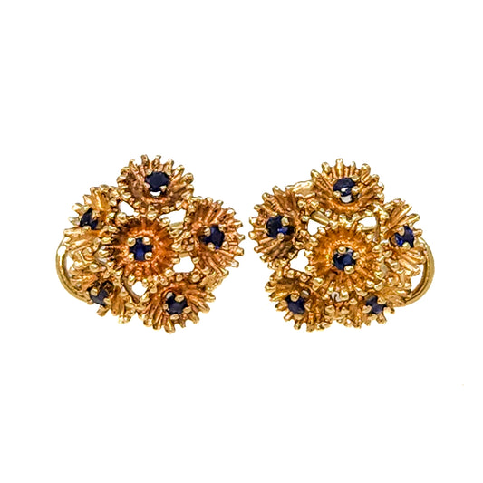 A pair of gold-toned floral hoop earrings with small dark blue gemstone accents, shown against a plain white background.