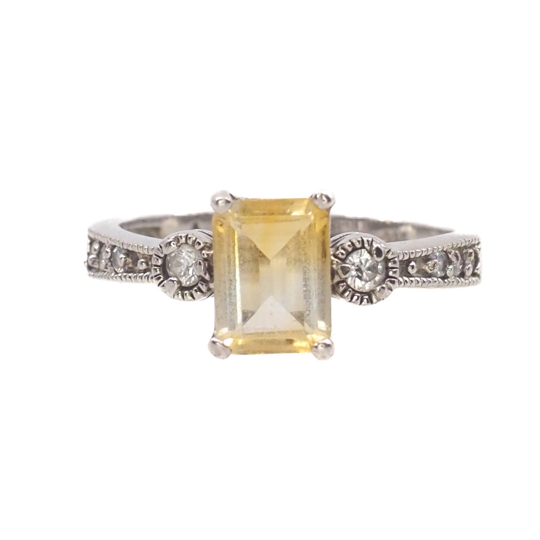 Silver ring with a yellow gemstone and smaller diamonds on a white background