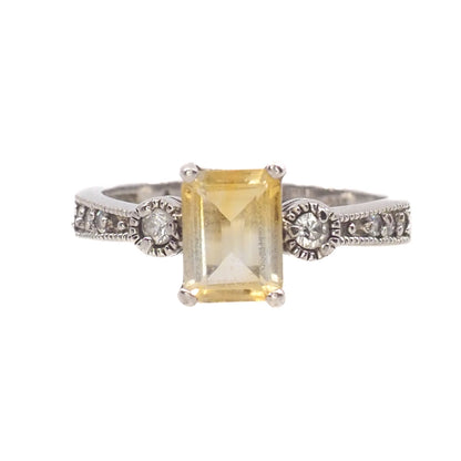 Silver ring with a yellow gemstone and smaller diamonds on a white background